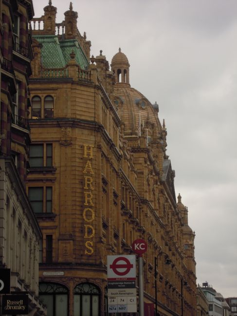 View of a historic London building with ornate architectural details, including decorative cornices and domes, situated on a busy street near a station entrance. In the foreground, a red and white rou